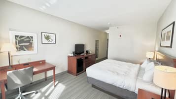 Habitación de hotel con cama, escritorio, silla, televisión y obras de arte en las paredes.