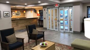 A lobby with two armchairs, a wooden reception desk, and a glass door with caution signs.