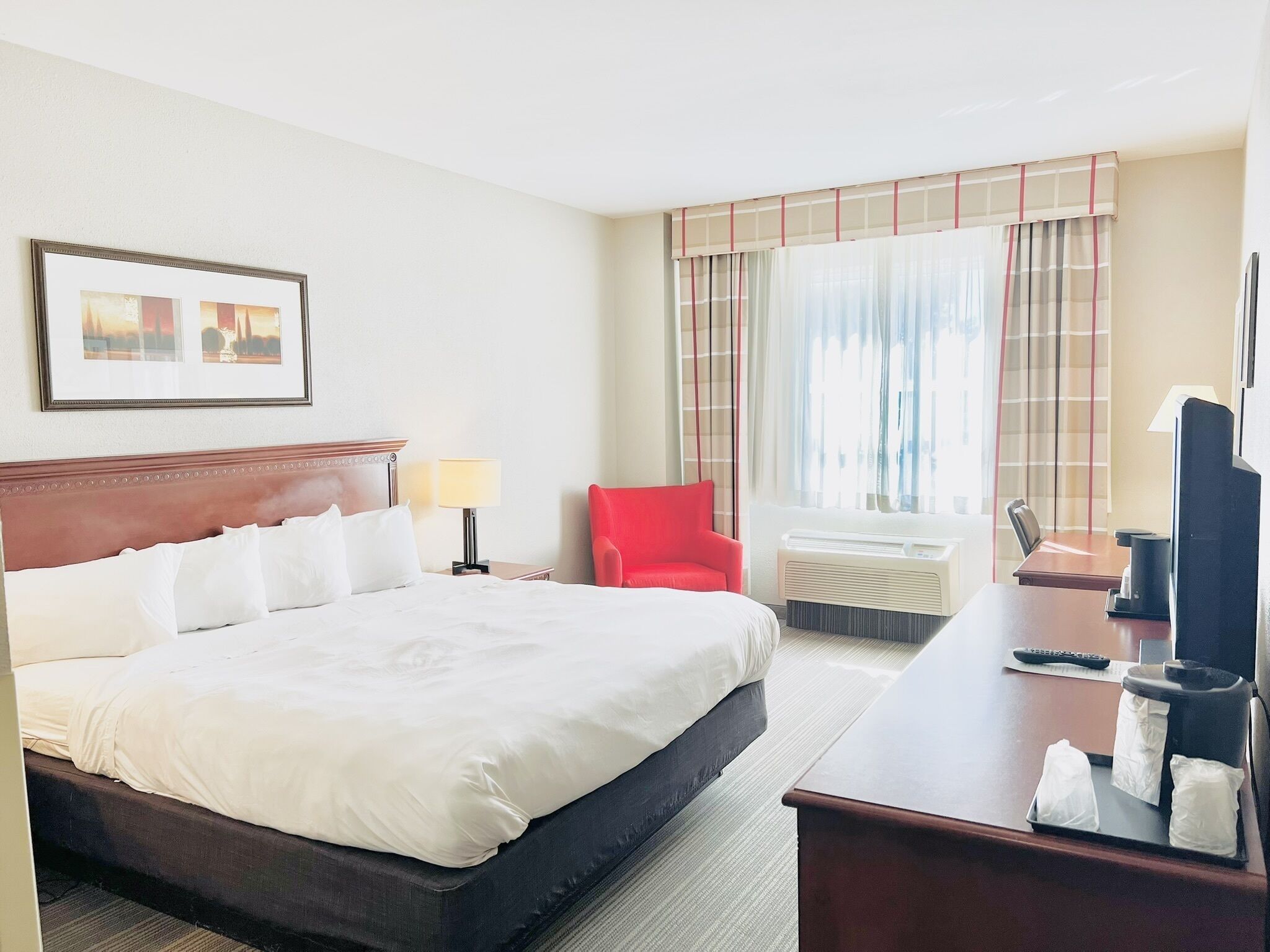 A hotel room with a large bed, a desk with a computer, a chair, a TV, and a window with curtains.