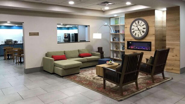 A modern living room with a sofa, chairs, a coffee table, a bookshelf, and a wall-mounted clock.