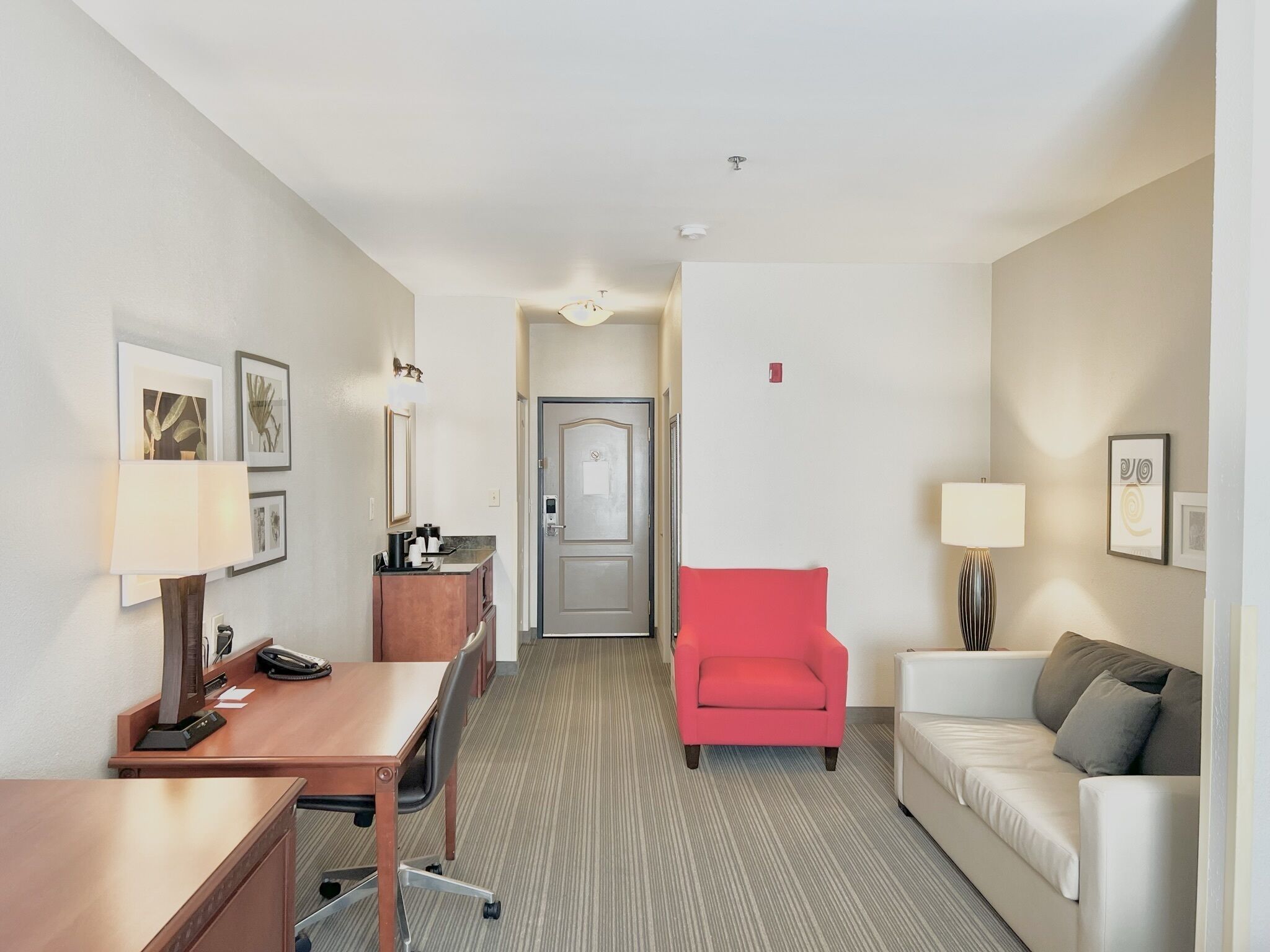 A hotel room with a desk, chair, sofa, and a door leading to another room.