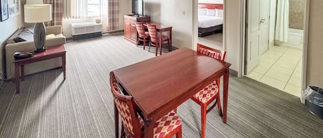 A hotel room with a dining table, chairs, a sofa, a TV, and a bathroom visible through an open door.