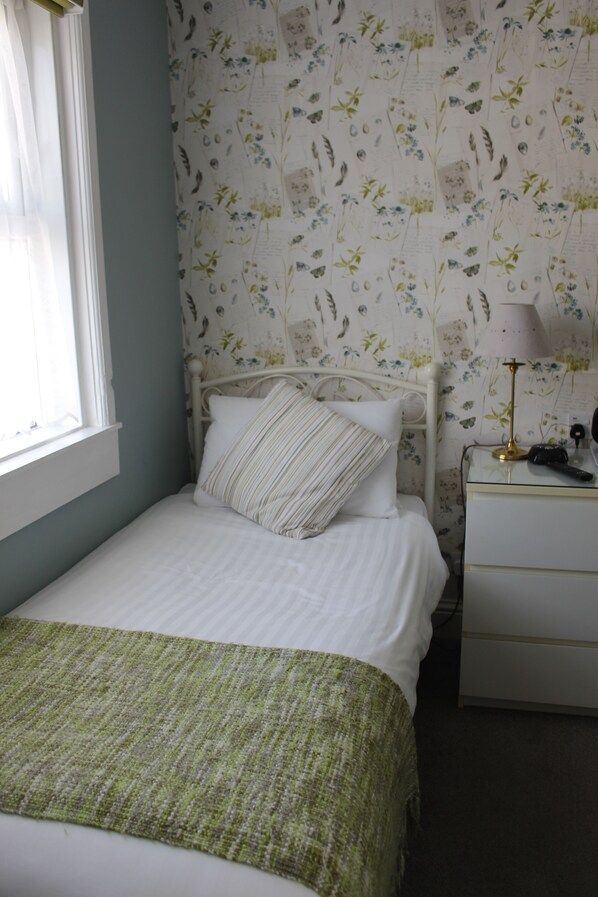 A neatly made bed with a green blanket, a white pillow, and a floral wallpaper pattern. - Beamsley Lodge (Eastbourne)