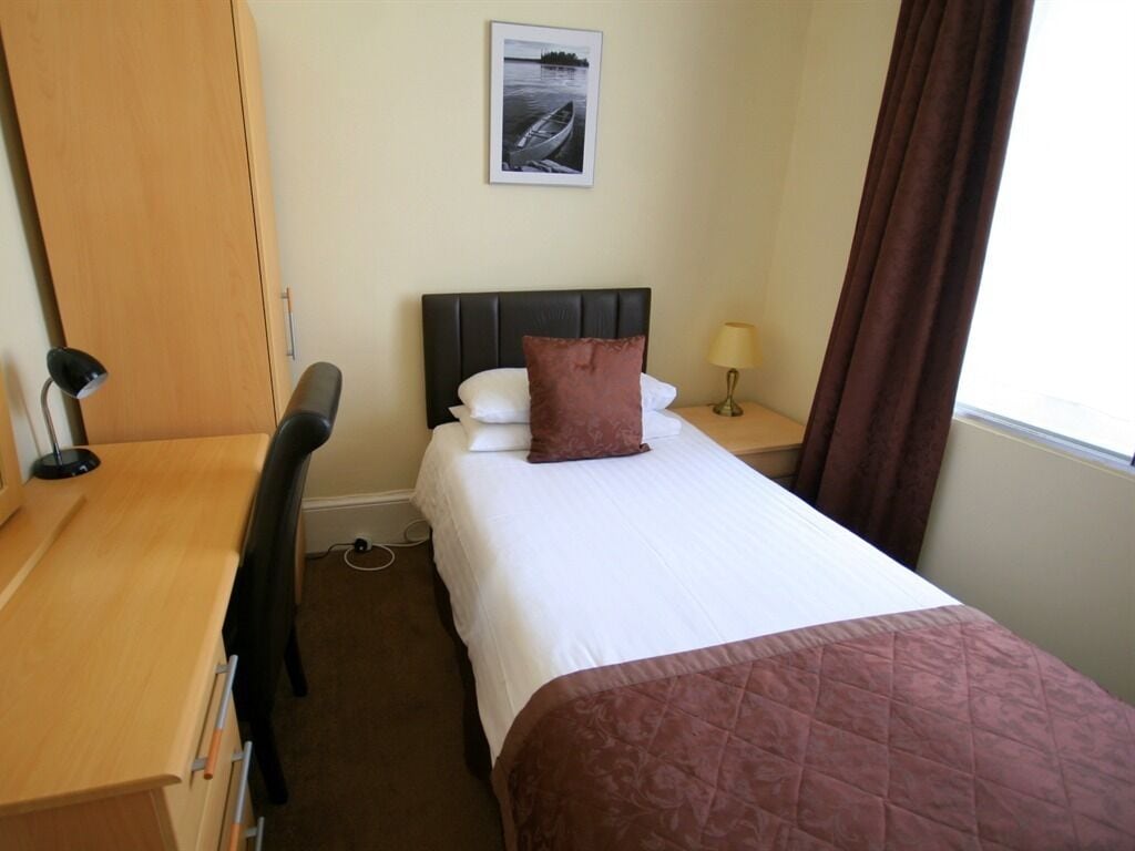 A hotel room with a bed, a desk, a chair, a lamp, and a picture on the wall.