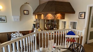 Un comedor con una mesa dispuesta para cuatro, una escalera de madera y una zona de bar al fondo.