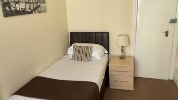 A neatly made bed with a brown blanket, a bedside lamp, and a small wooden nightstand.