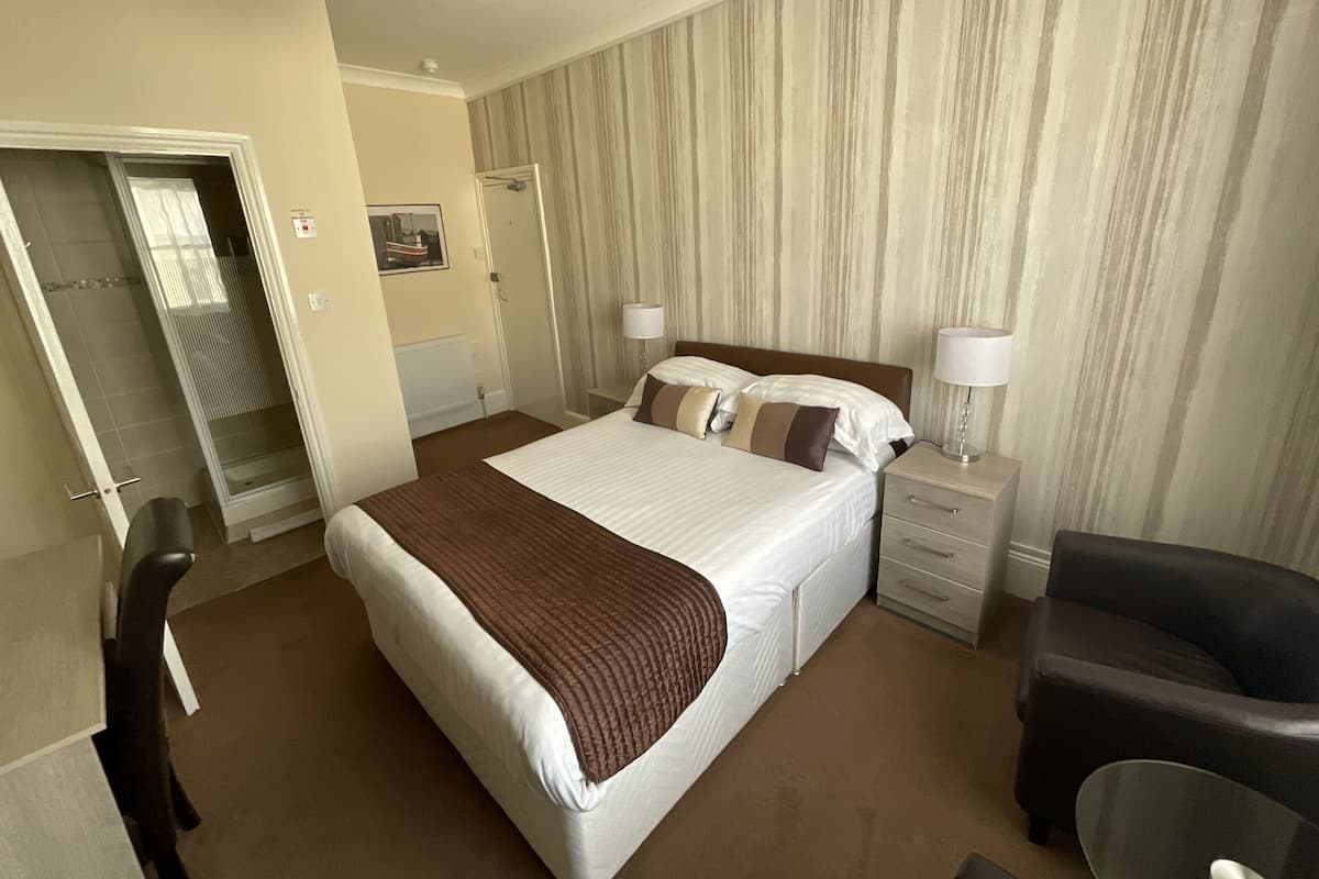 A hotel room with a large bed, a bedside table with a lamp, a chair, and a wardrobe.
