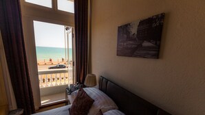Habitación de hotel con cama, un cuadro en la pared y vista a la playa a través de una ventana abierta.