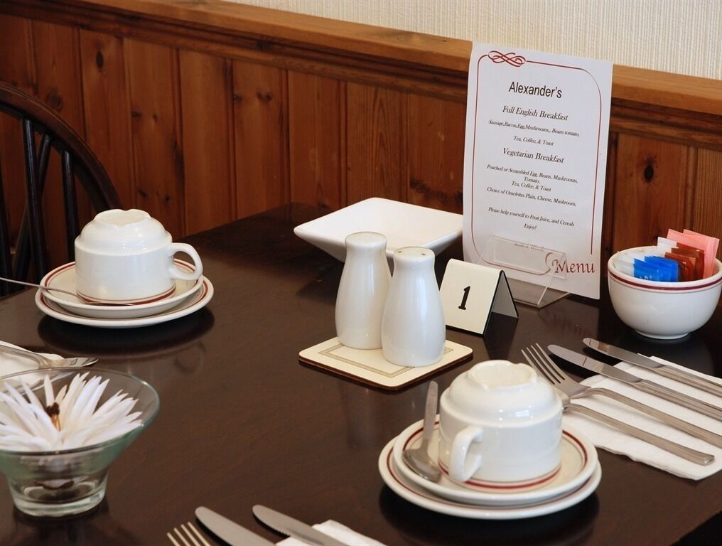 Une table à manger dressée avec des tasses et des soucoupes blanches, ainsi qu’un présentoir à menus.
