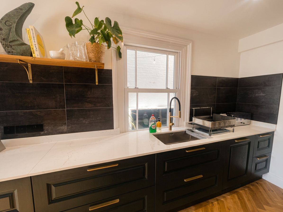 A modern kitchen with dark cabinetry, a white countertop, and a window.