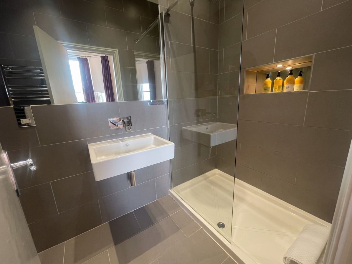 Un baño moderno con cabina de ducha de vidrio, un lavamanos blanco y un estante con artículos de aseo.
