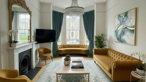 A living room with a fireplace, a television, a sofa, a coffee table, and a large painting. - Hastings House (St Leonards-On-Sea)