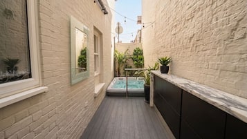 A narrow outdoor corridor with a wooden floor, a hot tub, and potted plants.