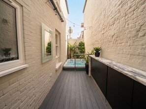 A narrow outdoor corridor with a wooden floor, a hot tub, and potted plants. - Hastings House (St Leonards-On-Sea)
