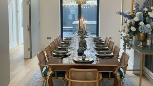 A dining room with a long table set for a meal, surrounded by wicker chairs with green cushions. - Hastings House (St Leonards-On-Sea)