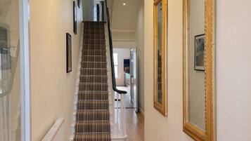 A hallway with a staircase, white walls, and a radiator.