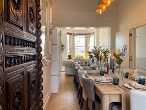 A dining area with a long table set for a meal, flanked by ornate wooden panels and a modern sofa.