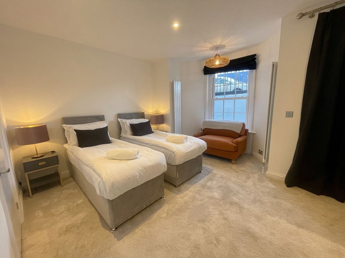 A bedroom with two beds, a nightstand, a chair, and a window with a view.