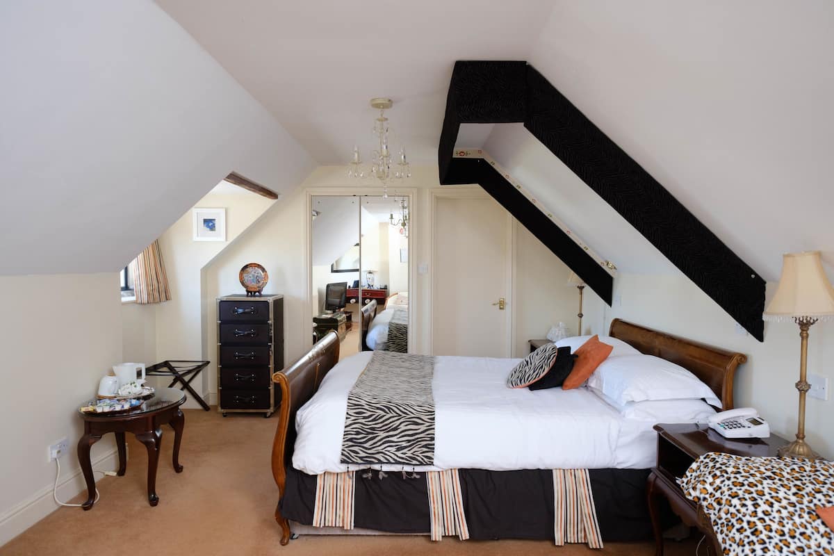 A bedroom with a large bed, a desk, a chair, a dresser, and a mirror.