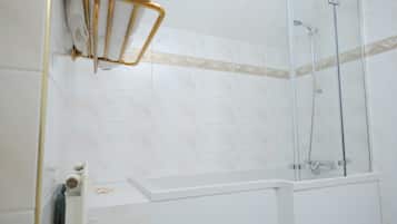 Casa de banho com azulejos brancos, cabine de duche em vidro e um porta-toalhas.