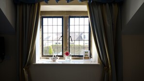 A window with a view of buildings outside, curtains, a vase with flowers, and a small table with a bowl and a brochure. - The Great House Hotel & Restaurant (Bridgend)