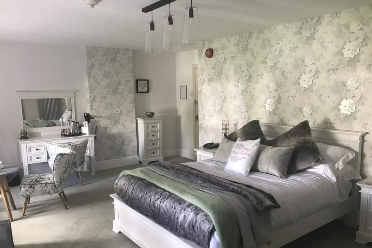 A bedroom with a large bed, a dresser, a vanity with a mirror, and a desk.