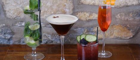 Three cocktails on a wooden table with a stone wall background.