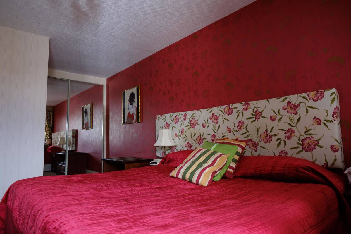 A bedroom with a large bed, floral wallpaper, and a mirror.