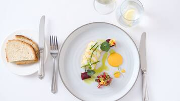 Una mesa de comedor blanca con un plato de comida, un vaso de agua y una copa de vino blanco.