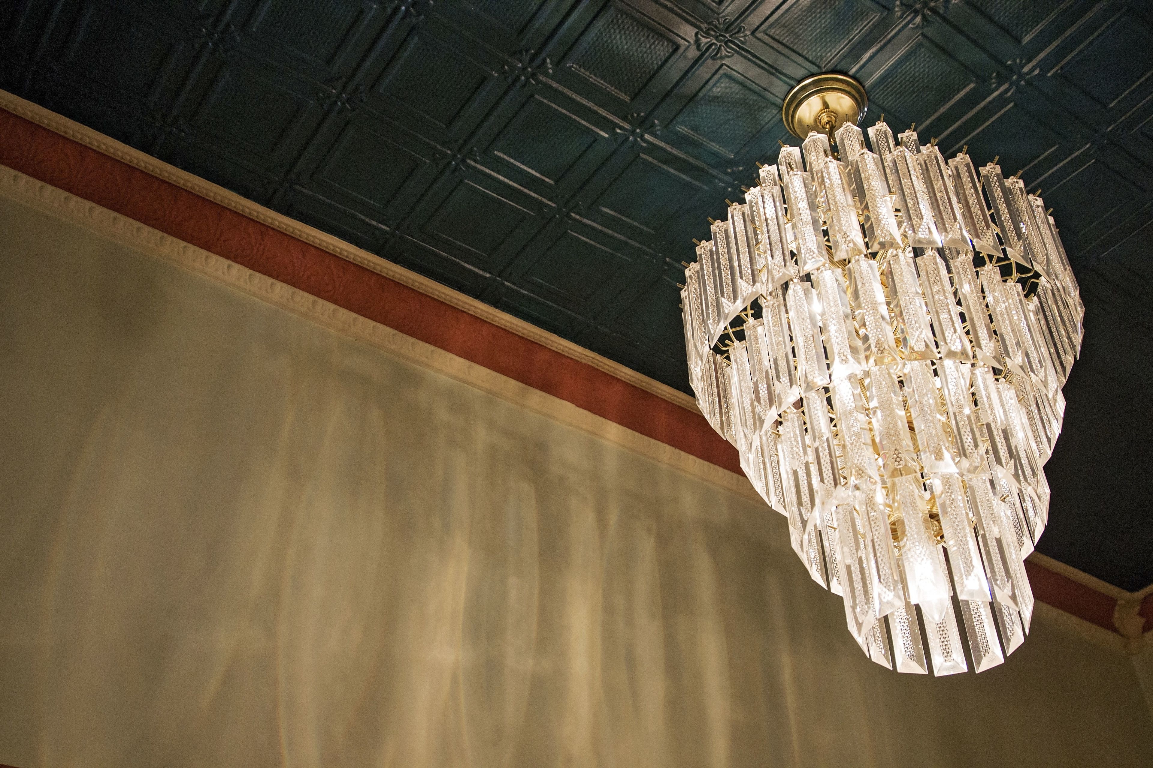 A chandelier with multiple tiers of crystal and gold accents, hanging from a dark, textured ceiling.