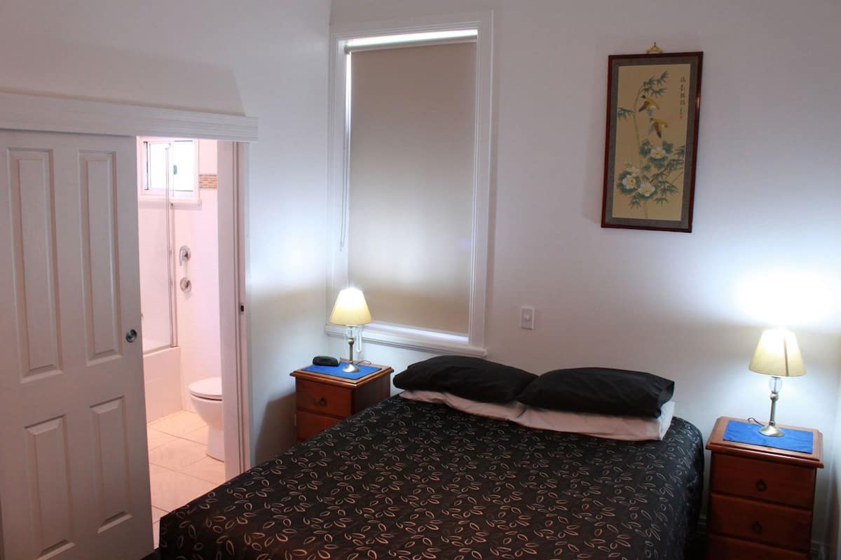A bedroom with a bed, two bedside tables with lamps, a window, a door, and a wall-mounted picture.