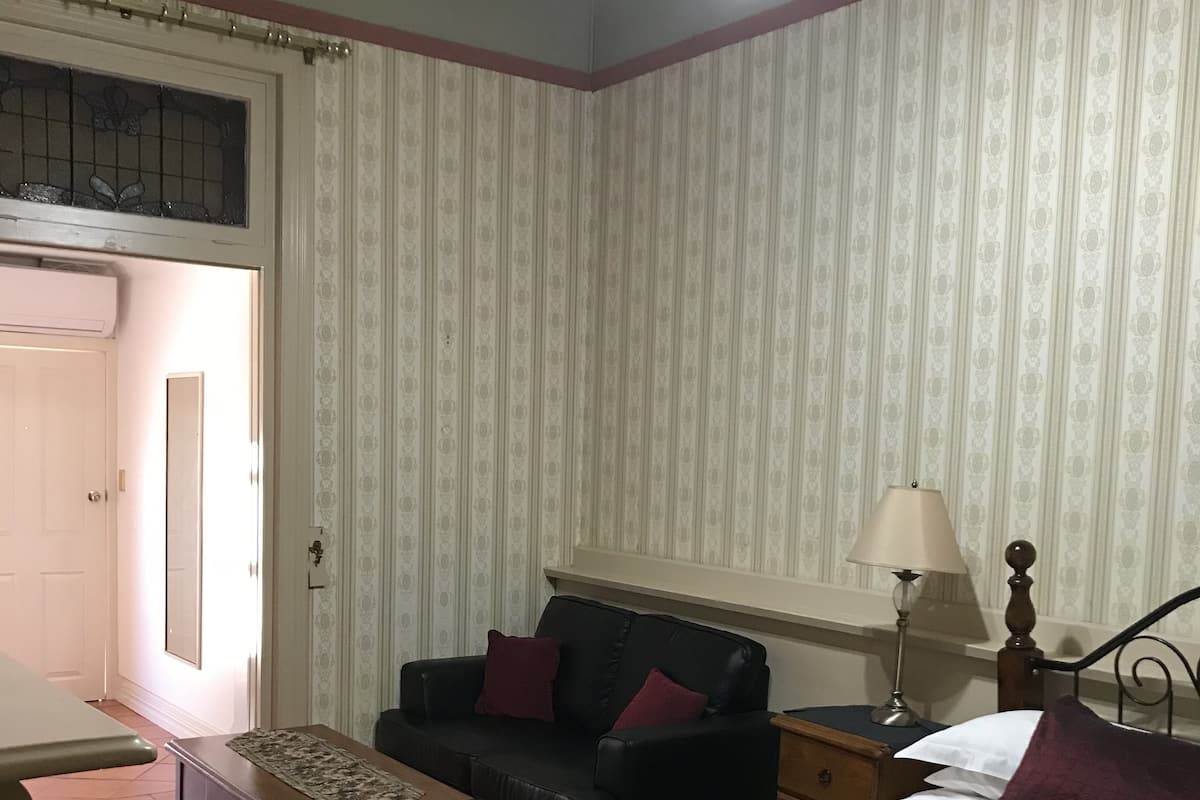A hotel room with a bed, a sofa, a small table, a lamp, and a window with curtains.
