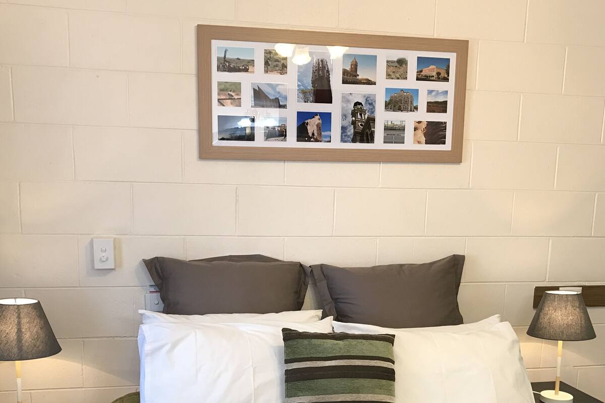 A neatly made bed with two pillows, a green blanket, and a framed photo collage on the wall above.