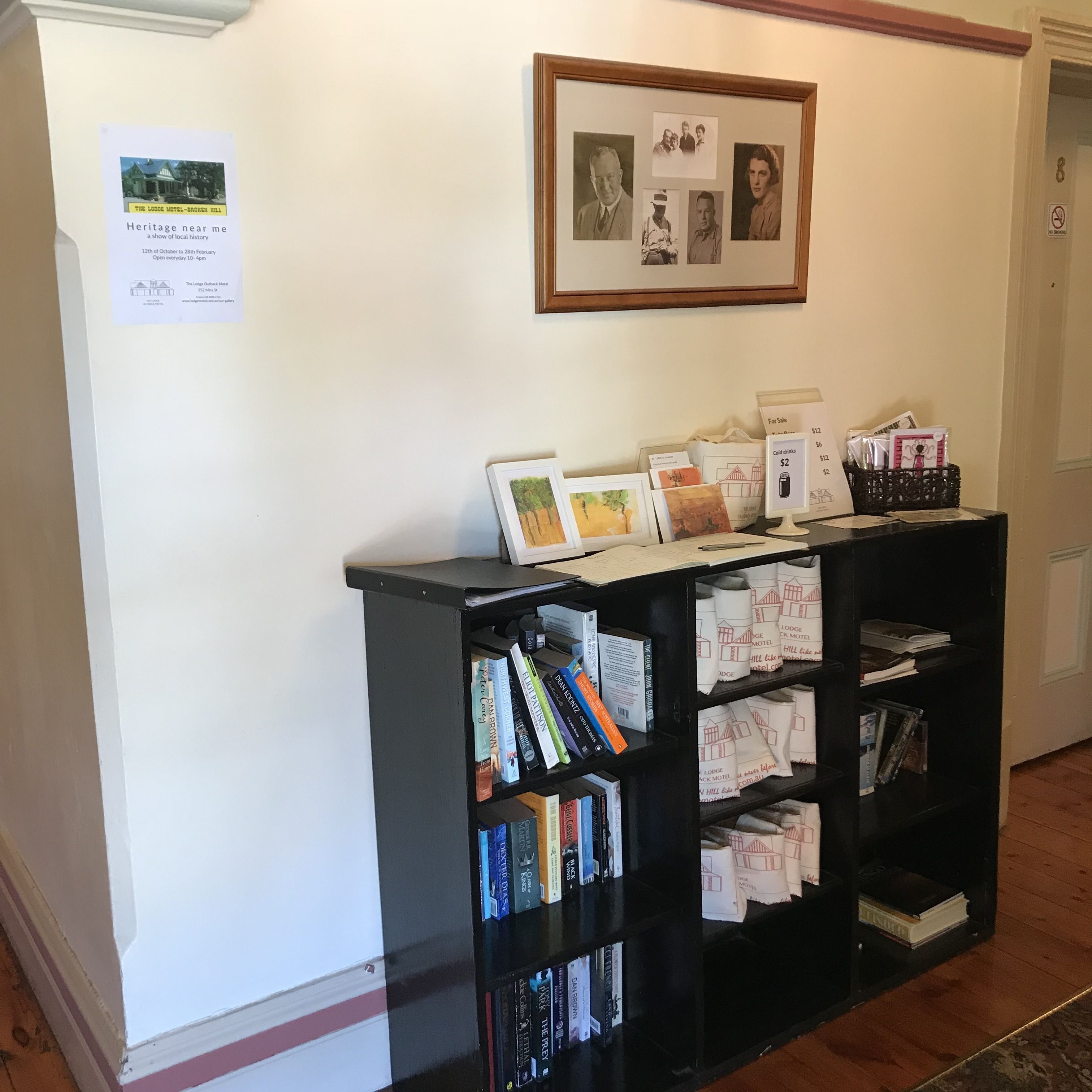 Una recepción con una foto enmarcada encima, un cartel con detalles de eventos, y una estantería llena de libros y material promocional.