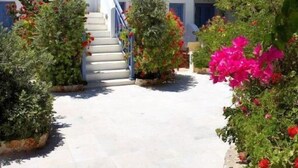 Ein weißes Gebäude mit blauen Fensterläden, einer Treppe und rosa Bougainvillea-Blumen.