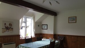 Comedor con mesa dispuesta para cuatro, paredes revestidas de madera, ventilador de techo y ventana con cortinas.