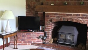 Una sala de estar con chimenea de ladrillo, televisor, alfombra escocesa y una mesa redonda de madera.