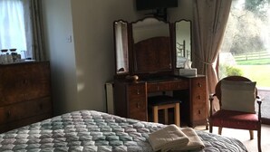 Un dormitorio con cama, cómoda, tocador con espejo, televisor en la pared y ventana con cortinas.