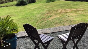 Un espacio al aire libre con dos sillas de madera y una mesa, rodeado por un muro de piedra y grava.