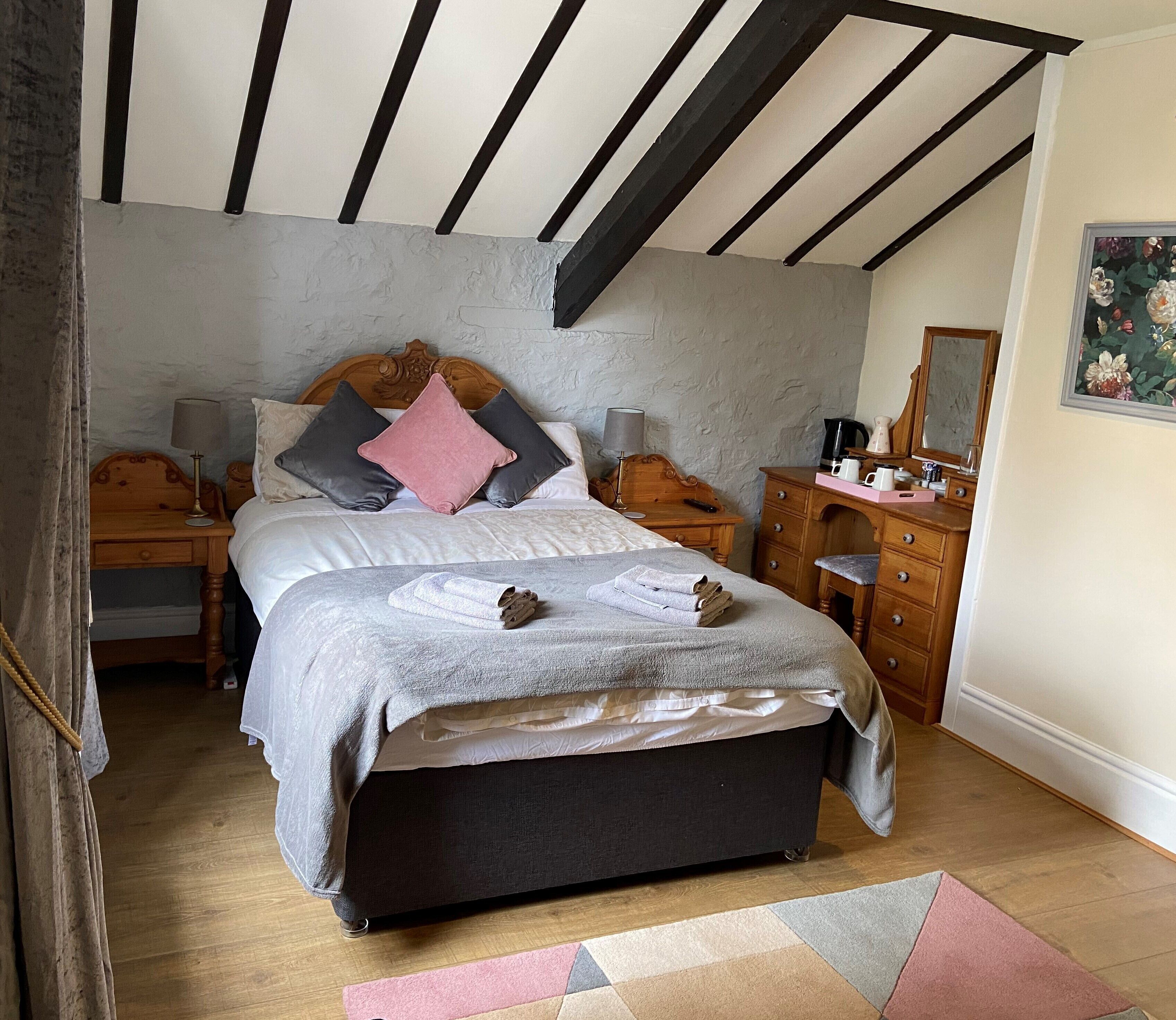 A bedroom with a large bed, wooden headboard, bedside tables with lamps, a dresser, and a painting on the wall.