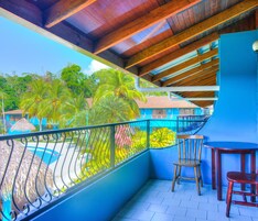 A balcony with a view of a swimming pool, palm trees, and a building with a red roof.