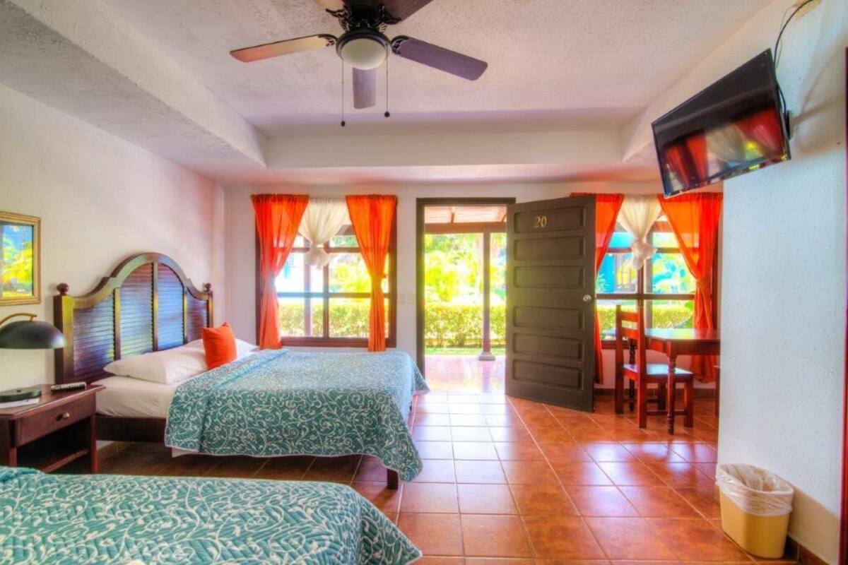 A hotel room with two beds, a ceiling fan, a TV, and a view of the outdoors.