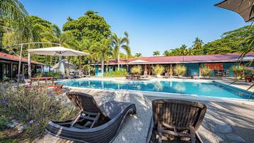 A pool area with lounge chairs, umbrellas, and a building with a red roof.
