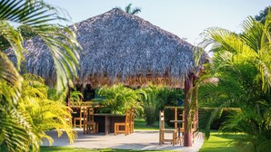 A thatched-roof structure with outdoor seating and lush greenery. - Beach Break Resort (Jacó)