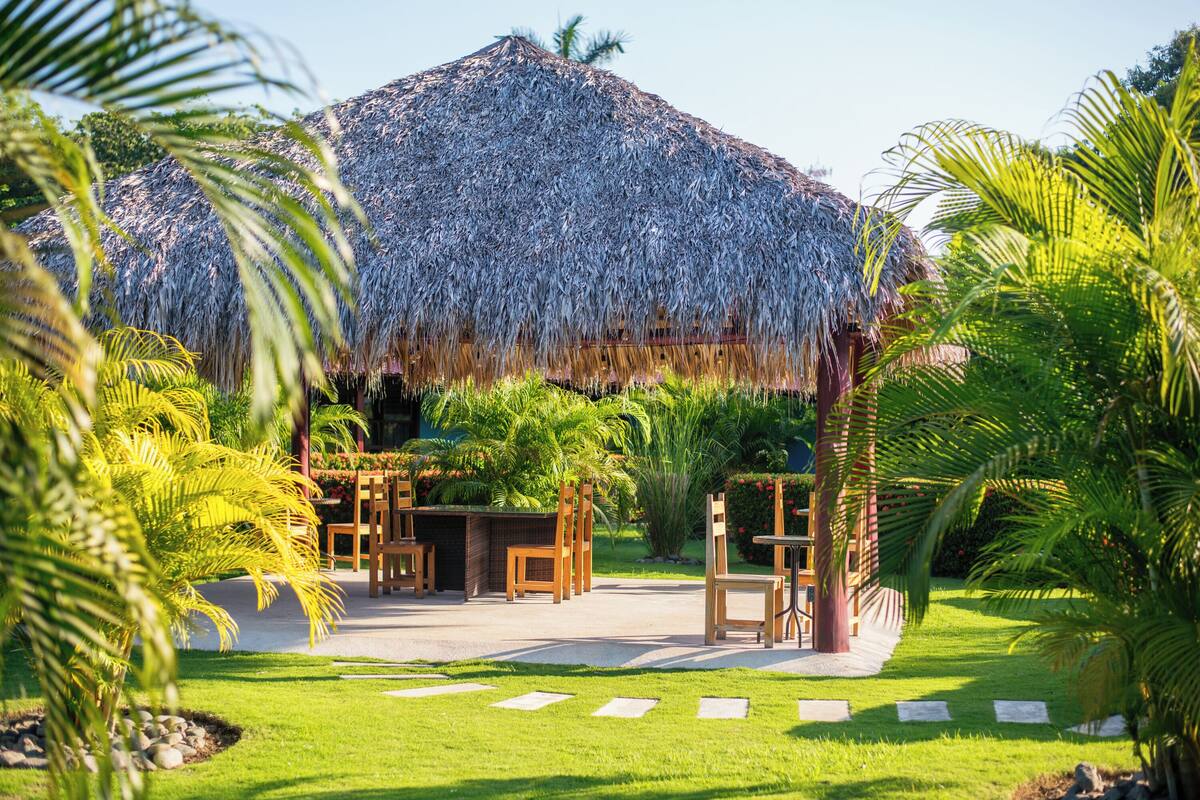 A thatched-roof structure with outdoor seating and lush greenery.