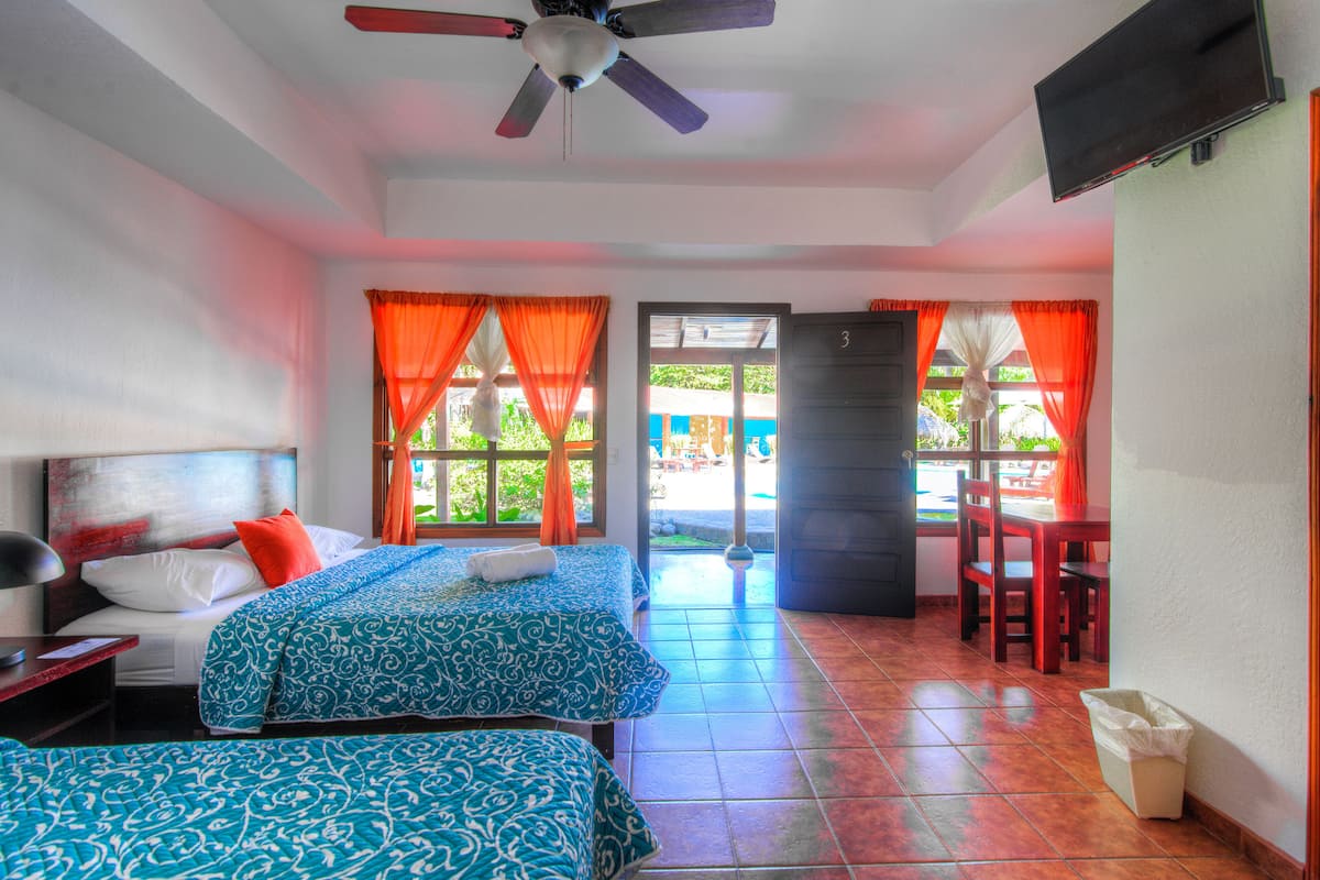A hotel room with two beds, a ceiling fan, a TV, and a view of the outside.