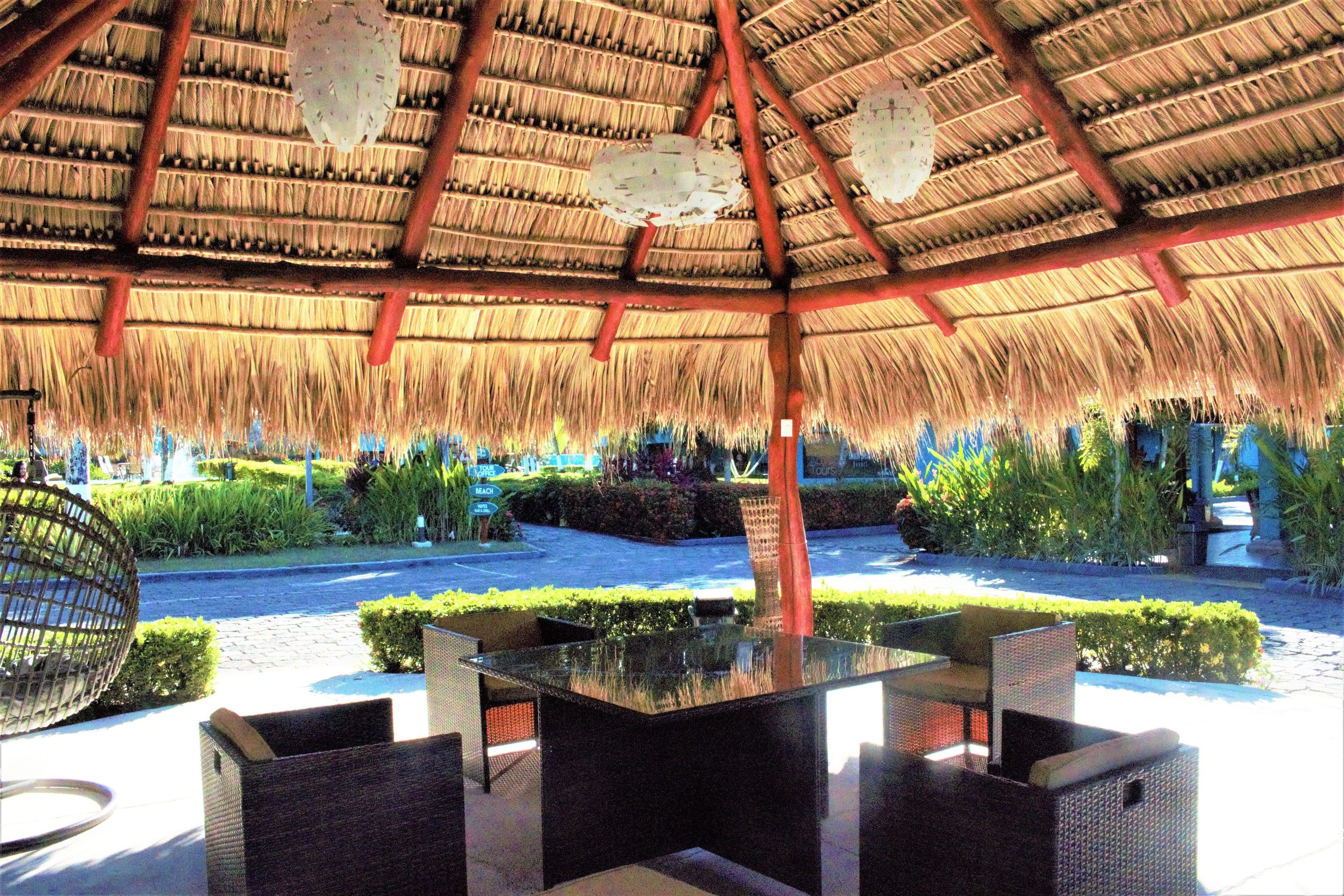 An outdoor seating area with a thatched roof, wicker furniture, and a well-maintained garden.