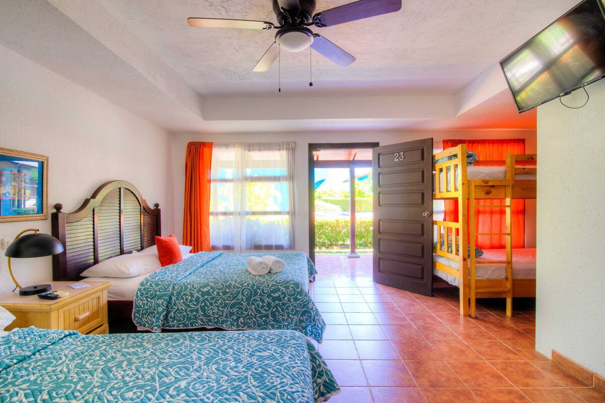 A hotel room with two beds, a ceiling fan, a TV, and a view of the outdoors.