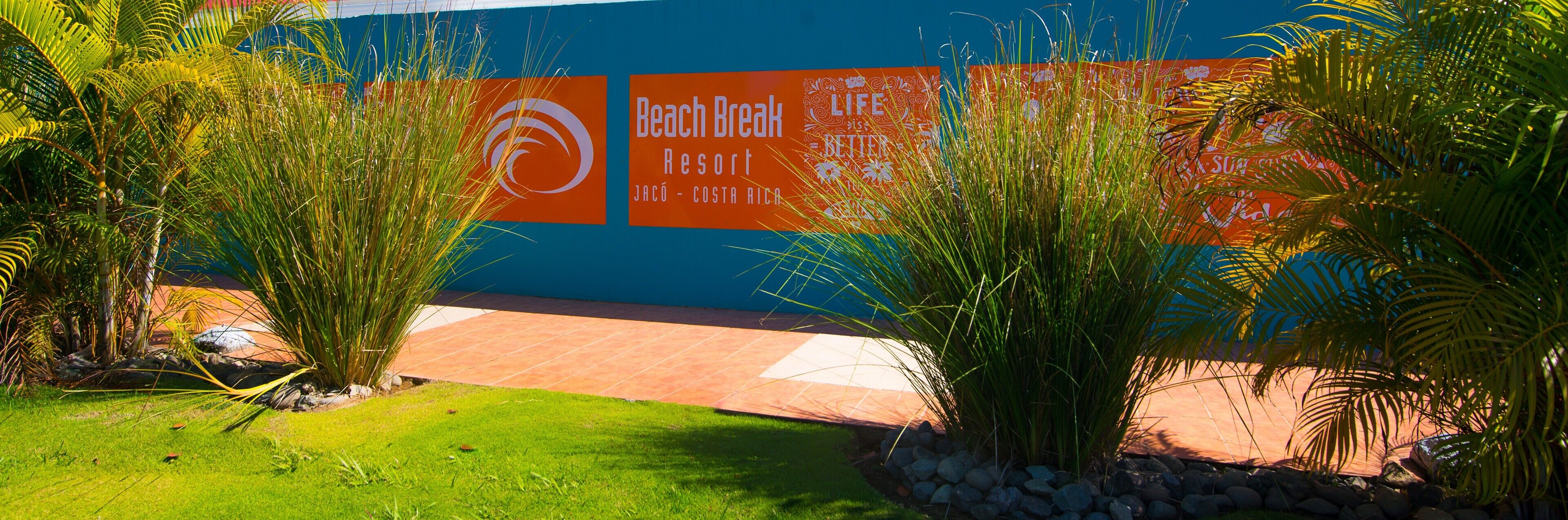 Entrada a un resort con una pared azul y un letrero naranja que dice 'Beach Break Resort Jacó - Costa Rica'.