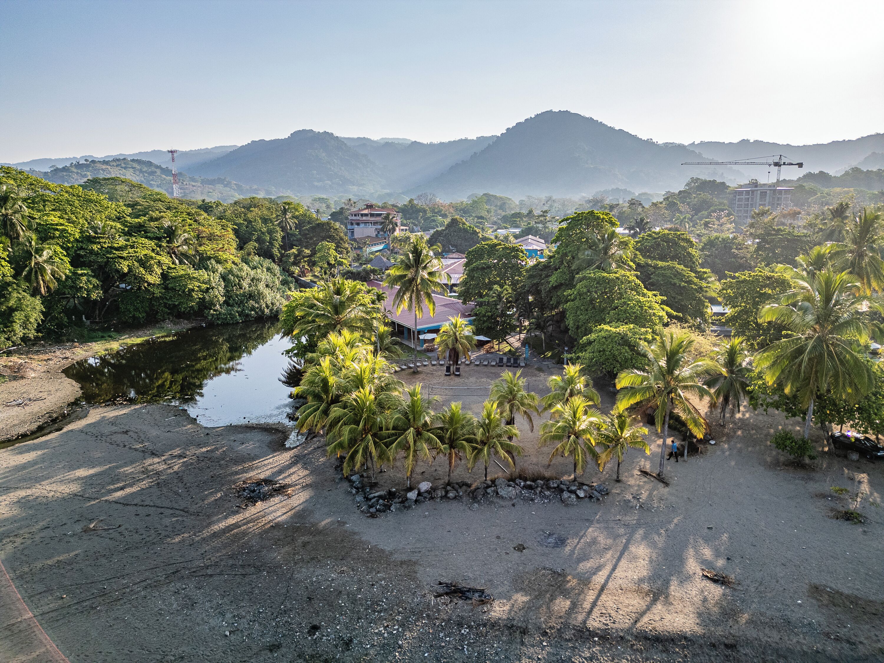 Zona costera con playa, palmeras, un edificio pequeño y un río.